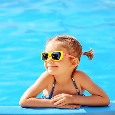Egy kisgyermek mosolyog a medence szélén. A medencék vizének keménysége károsíthatja a medence felületét és korrodálhatja a csővezetékeket.